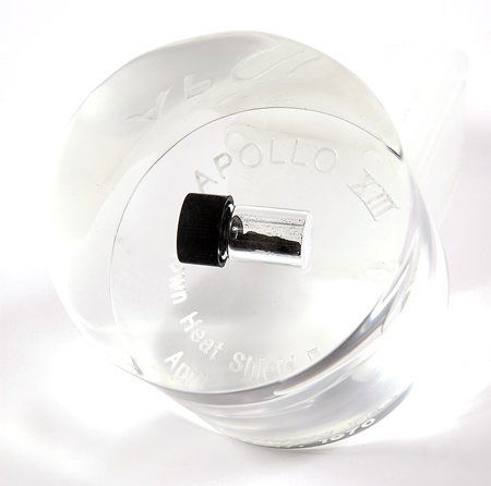 Apollo 13, 1970, Flown Heatshield Fragments: Apollo 13, 1970, Flown Heatshield Fragments. A small vial of charred heatshield fragments mounted in a clear lucite cylinder (3x3") that is engraved on the bottom: "Apollo XIII / Flown