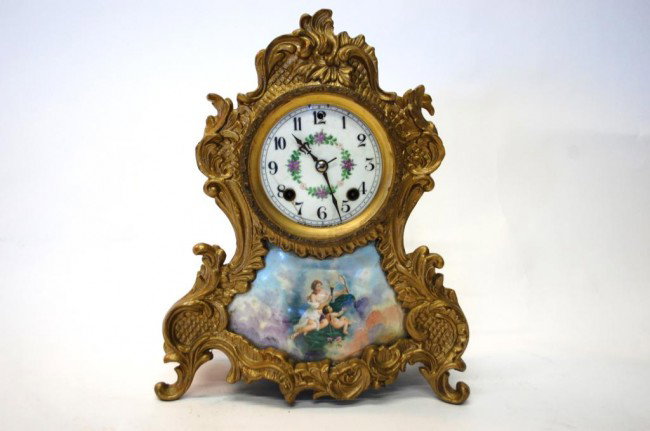 New Haven Gilt French Style Shelf Clock: Porcelain dial w/ painted flowers, porcelain hand-painted Panel below dial depicting woman with torch in the company of an angel. Dial with two short cracks. Glass missing from bezel. 12 3/4" tall.