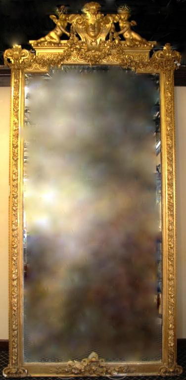 Louis XVI 19th Century French Gilt Trumeau Mirror: Monumental Mirror with beveled glass, crowned by two angels flanking a central figure, rose garland swags, and intricate detail along the entire perimeter terminating in a central bow at the bottom. M