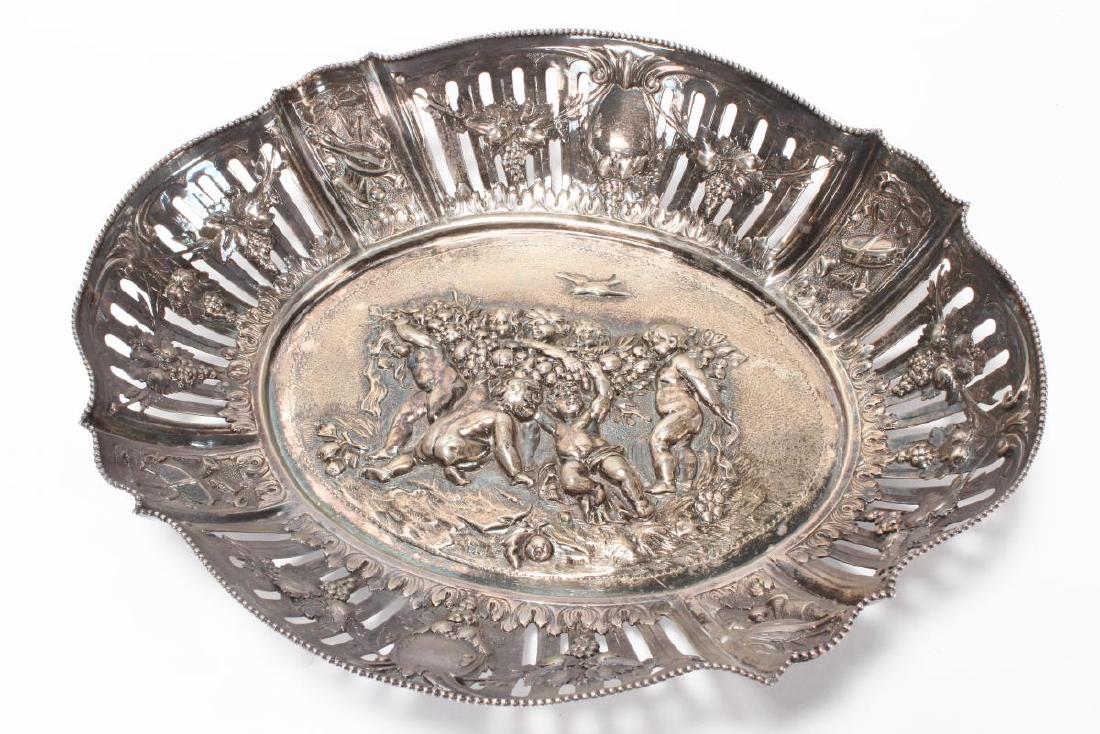 German Hanau Silver Twin Handled Dish,: hallmarked, Karl Söhnlein & Söhne, of oval form with a beaded serpentine rim, decorated with embossed cherubs to the centre and grapevines and musical instruments to the edges, a/f, total weight 430