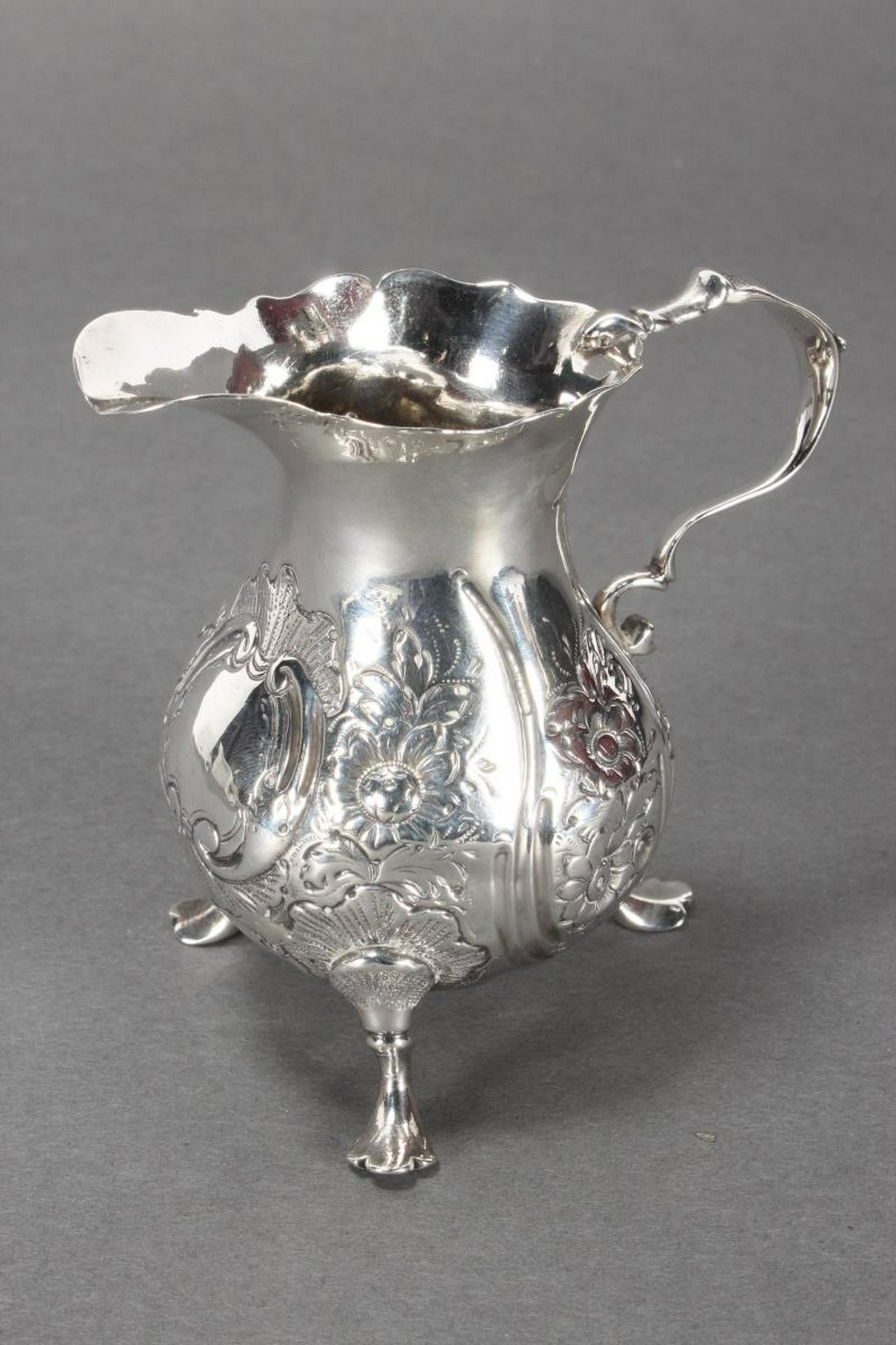 George III Sterling Silver Footed Creamer,: hallmarks rubbed, with shaped spout, above a baluster body, embossed with cartouche and floral motifs, on three feet, total weight 81gm, l 8.5cm