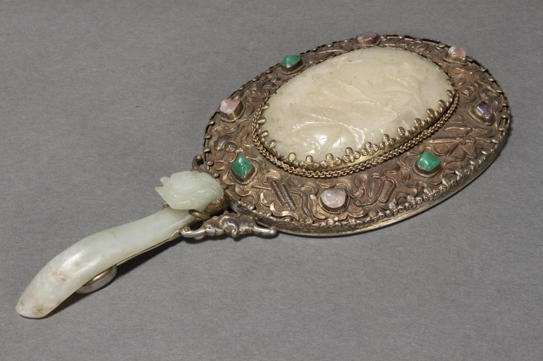 Chinese 19th Century Jade Mirror,: the silvered frame decorated in repousse with Buddhist symbols set with central oval jade panel, carved with bird, flowers and foliage, accented with coloured stones, with jade figural handle, length 