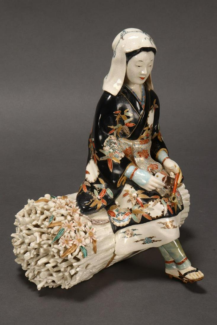 Japanese Meiji Period Kutani Figure Group, c.1870,: depicting a seated lady in elaborate kimono filling a pipe, seated upon a faggot of sticks, in rich tones of blue, red, gold and black, seal mark Kenzan, a/f, 18cm x 23cm