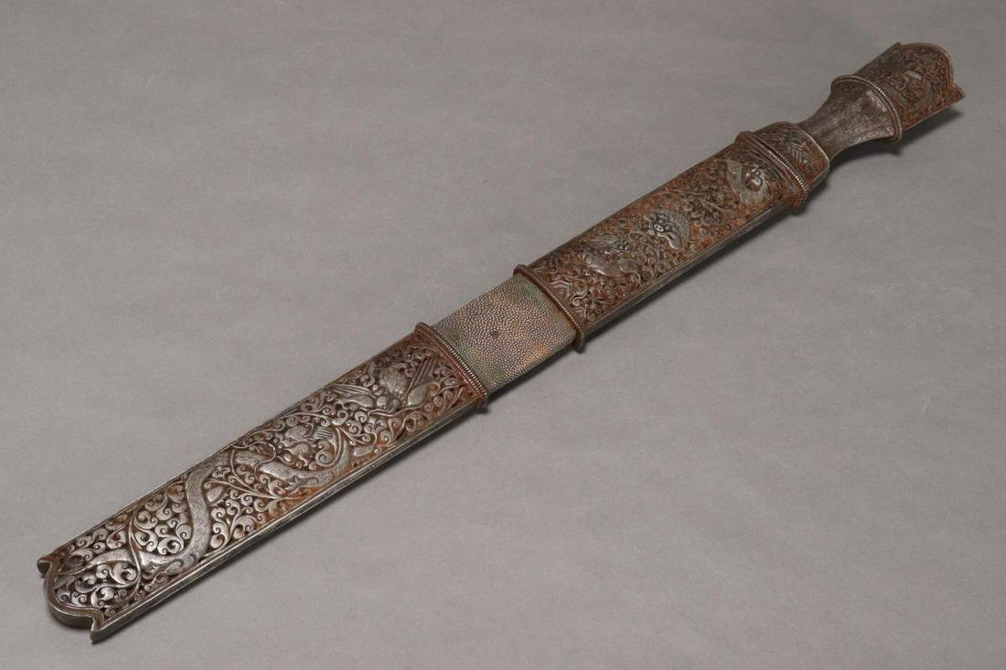 19th Century Tibetan Silvered and Shagreen: Covered Sword, the sheath and hilt cast with dragon and mythical beasts on an ornate vine and lotus ground, bisected by a shagreen band, enclosing a blade with copper inlay to the tip, inscribed 'Tash