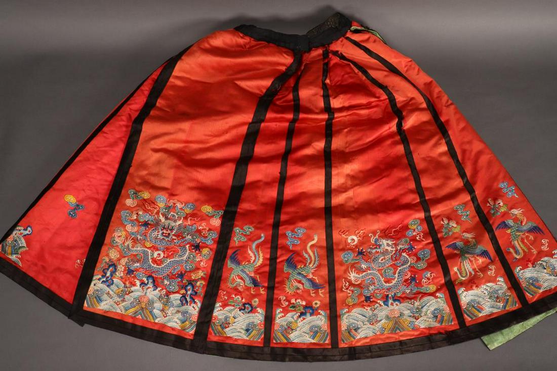 Chinese Late Qing Dynasty Winter Skirt,: padded, embroidered with dragons and phoenix amongst stylised clouds and turbulent waves, in tones of blue, green and yellow on a red ground, with black trim and pale green lining, length 79cm