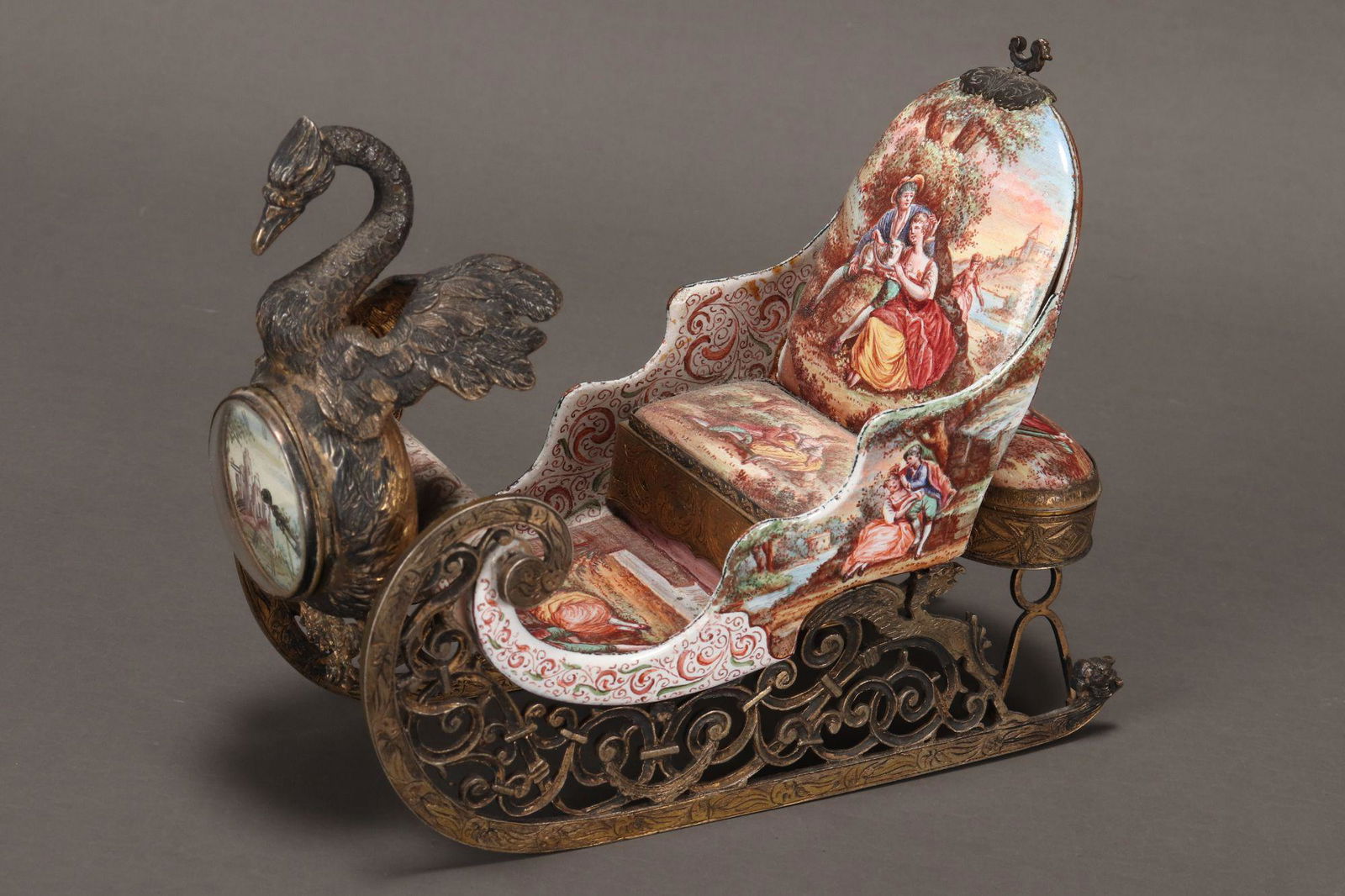 Viennese Enamel and Gilt Silver Sleigh Clock,: the circular dial with Roman numerals and hand painted castle scene set within a swan figurehead, the sleigh decorated with hand painted scenes after Jean Antoine Watteau, with pill box set to the bac