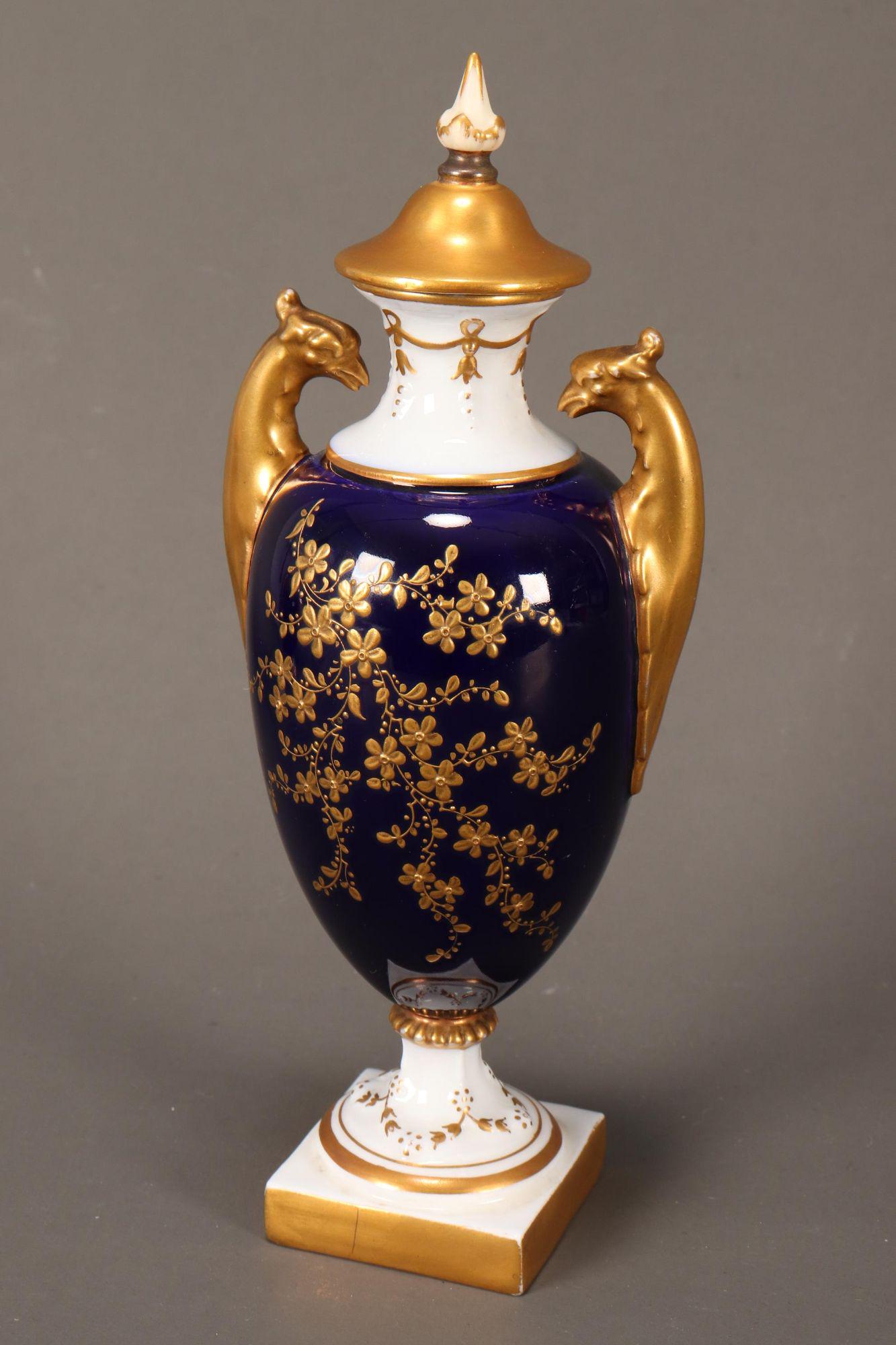 Royal Worcester Twin Handled Vase and Cover,: with twin phoenix handles, the body decorated in gilt with flowers and foliage, with gilt cover and pointed finial, raised on a square base, in cobalt, white and gilt, green factory stamp to base, hei
