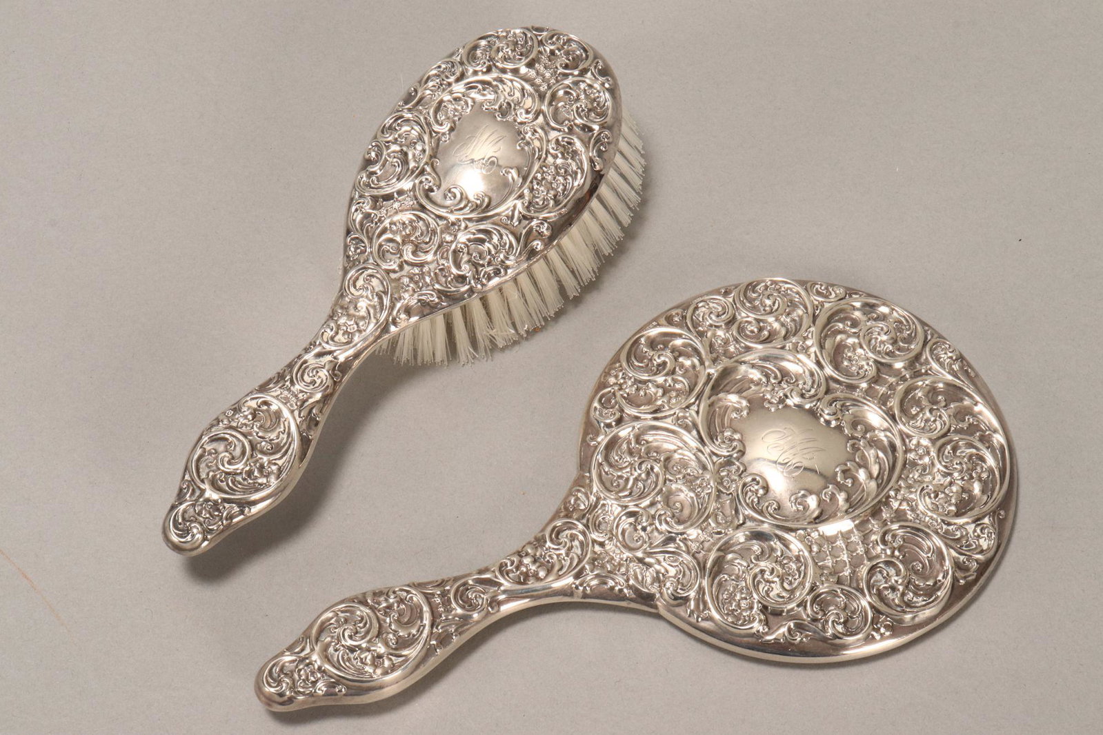 Canadian Sterling Silver Hand Mirror and Brush,: marked Birks, decorated with central cartouche engraved with monogram surrounded by embossed acanthus, c-scrolls and flowers, length 25cm and 21.5cm (2)