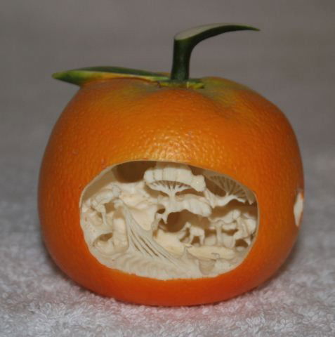 Japanese Stained Ivory Figure of a Tangerine,: pierced to one side with a scene of sail makers on a rocky outcrop, d 5.5cm, h 5cm