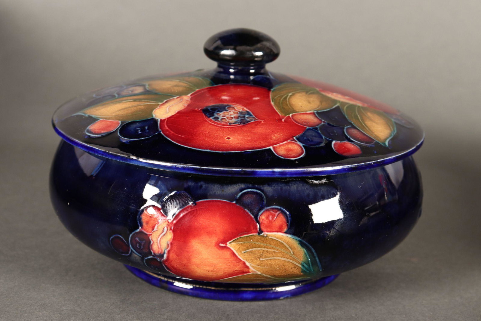 William Moorcroft 'Pomegranate' Jar and Cover,: c.1928-49, the body of squat circular form with a slightly domed cover and finial, decorated with pomegranates and berries on a rich royal blue ground, with impressed signature, 'Potter to H.M The Que