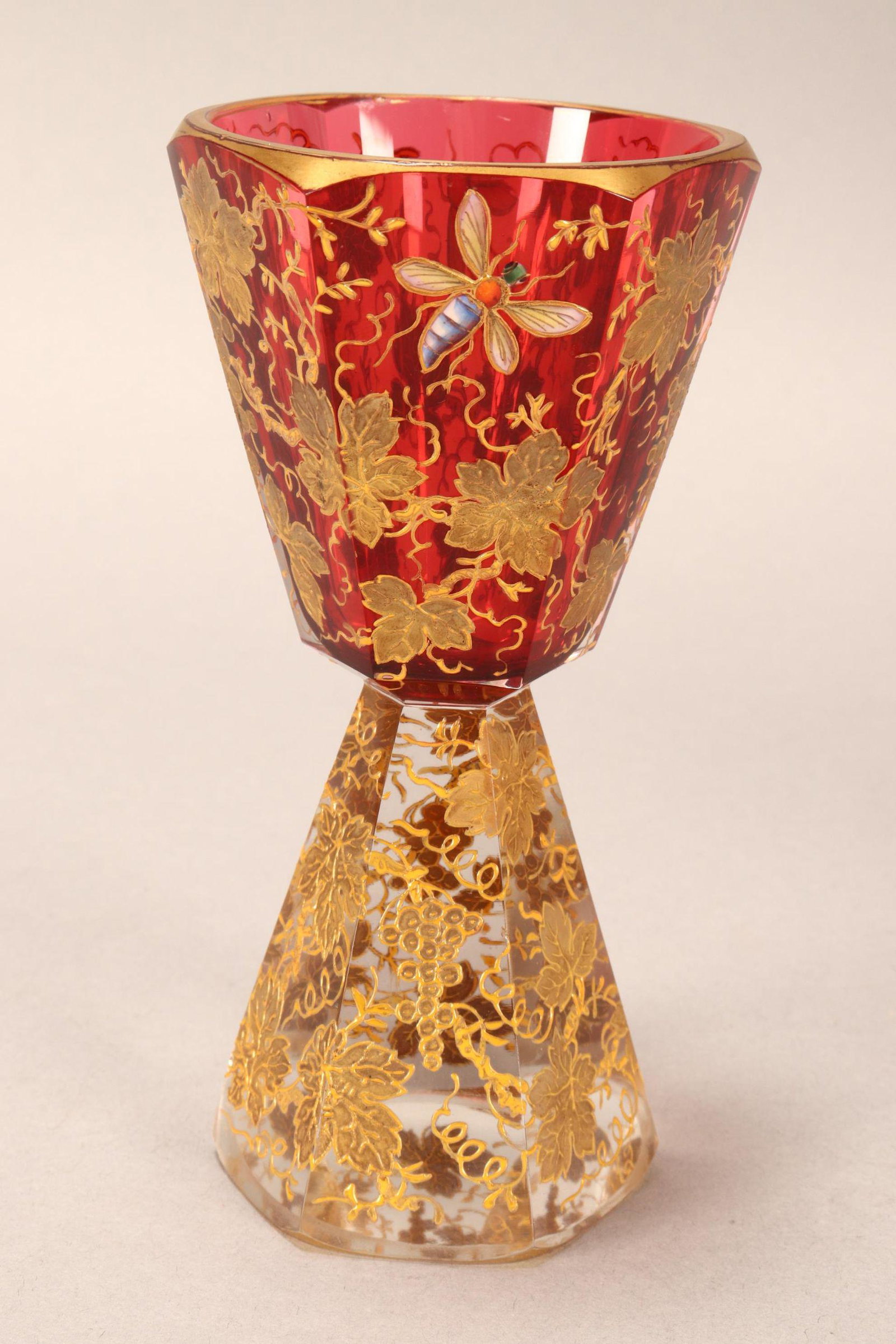 19th Century Moser Glass Goblet,: of facetted form above a heavy facetted base, in ruby and clear glass, decorated with enamelled insects and continuous gilt grapevine motif, height 14cm