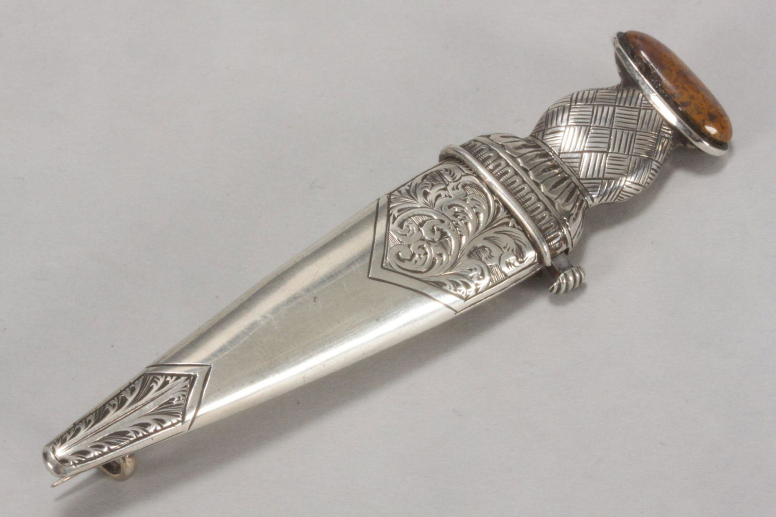 Victorian Scottish Silver Dirk Kilt Pin,: unmarked, registered design m 21gm, length 9.5cmark verso c1876, of Dirk dagger form with foliate engraved sheath, cross hatched handle and stone set pommel, with spring push button release revealing