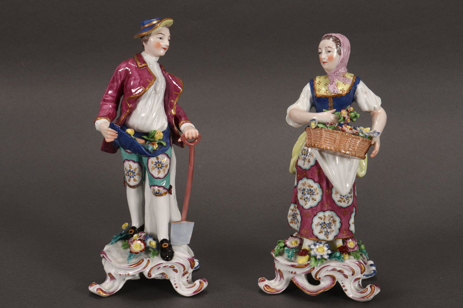 Pair of 19th Century English Porcelain Figures,: depicting a man with fruit and shovel and a woman with a basket of flowers, with encrusted flowers to base, a/f, in tones of purple, blue, yellow and green, red anchor and cross mark to base, height 2