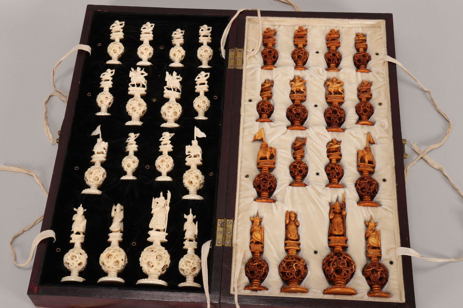 Chinese Carved Chess Set,: each piece carved with sword wielding figures and elephants above a puzzle ball base, one side natural, the other stained yellow, height 14cm (king) and 8cm (rook), with original board with fitted and