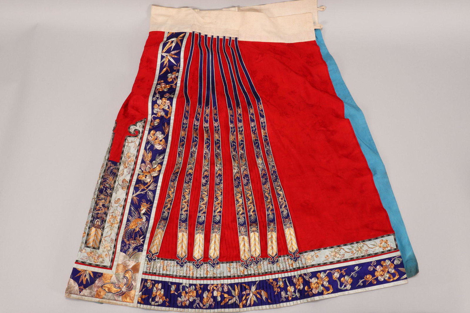 Luxurious Chinese Embroidered Wedding Skirt,: in red silk, heavily couched in gold and silver thread with phoenix, peonies, butterflies and dragon on a dark blue and pale green satin ground, accented with couched tassels, with white cotton waistb