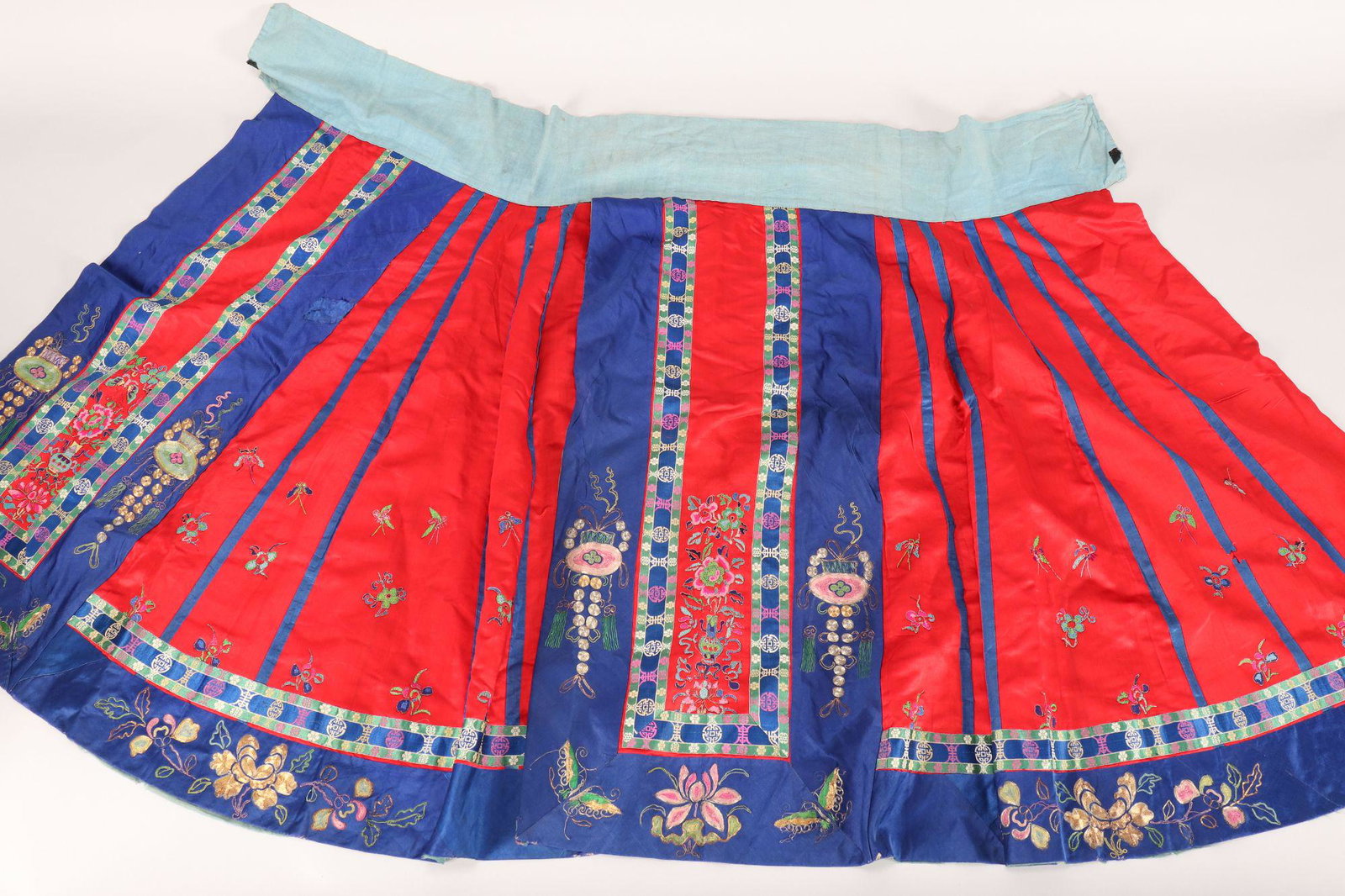 Chinese Embroidered Satin Skirt,: embroidered in Peking knot with vases, flowers and butterflies, couched in gold and silver thread with lanterns, flowers and butterflies on a red and blue satin ground, with pale blue cotton waistband