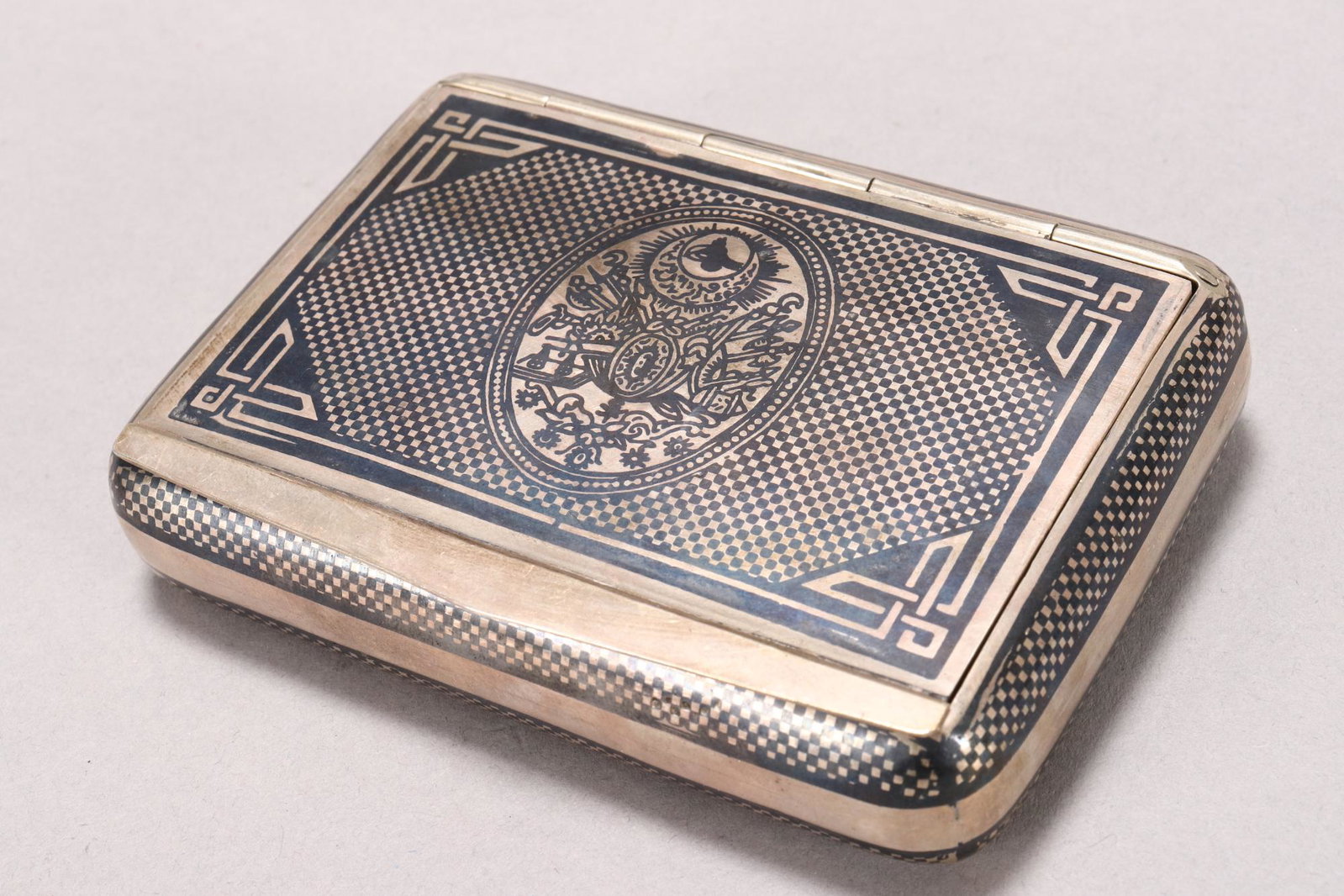 Van Turkish Silver Niello Cigarette Box and Cover,: marked Van and script, of handsome pillow form, with inset cover, decorated with armorial, surrounded by checkered ground, the back with reserve surrounded by flowers and checkered ground, total weigh