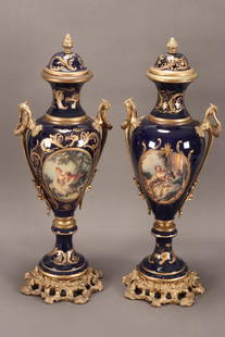 Pair of Sevres Porcelain and Gilt Lidded Urns,: of handsome proportions, of classical form, decorated with roundels of courting couples, surrounded by gilt scroll and acanthus work, on a cobalt ground, flanked by gilt handles and gilt rococo style