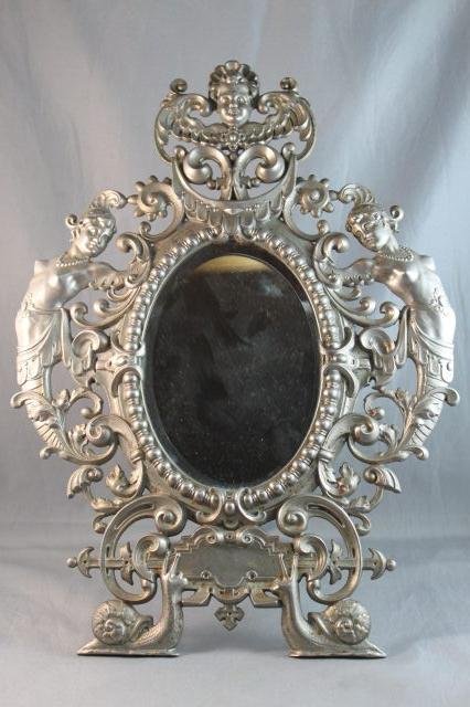 Good German Gesetzlich Classical Table Mirror,: with a central oval bevelled mirror, surrounded by cherub masks, classical maidens and strap work, the whole resting on a pair of cast snails, h 34cm