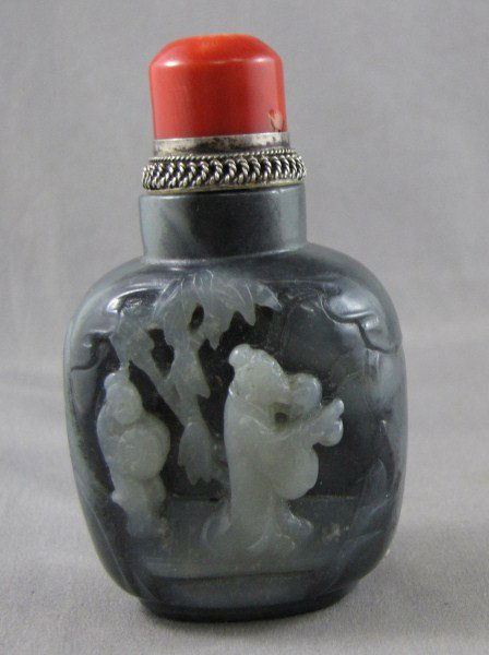 Chinese Black and White Snuff Bottle and Stopper,: of baluster form, each side carved with scholars and figures, within a landscape, with coral stopper, h 8cm