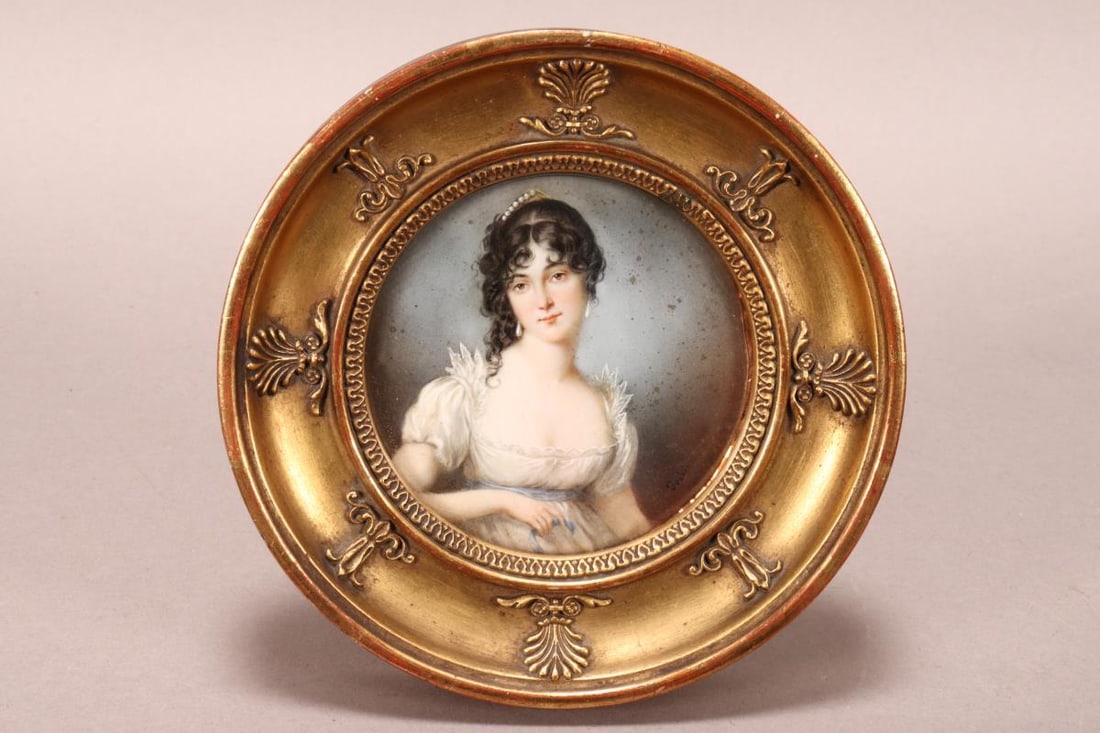 19th Century Portrait Miniature,: of roundel form, depicting a lady seated in three quarter with head turned wearing pearl headdress and earrings, with lace dress tied with blue ribbon, set within a gilt frame, diameter 14.5cm