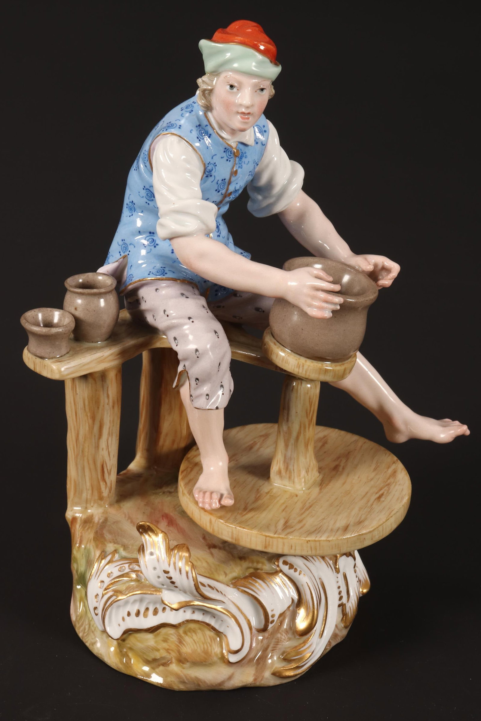 Meissen Porcelain Figure of a Potter,: depicted seated and throwing a pot at wheel, in tones of blue, orange and mauve, accented with gilt, height 19cm