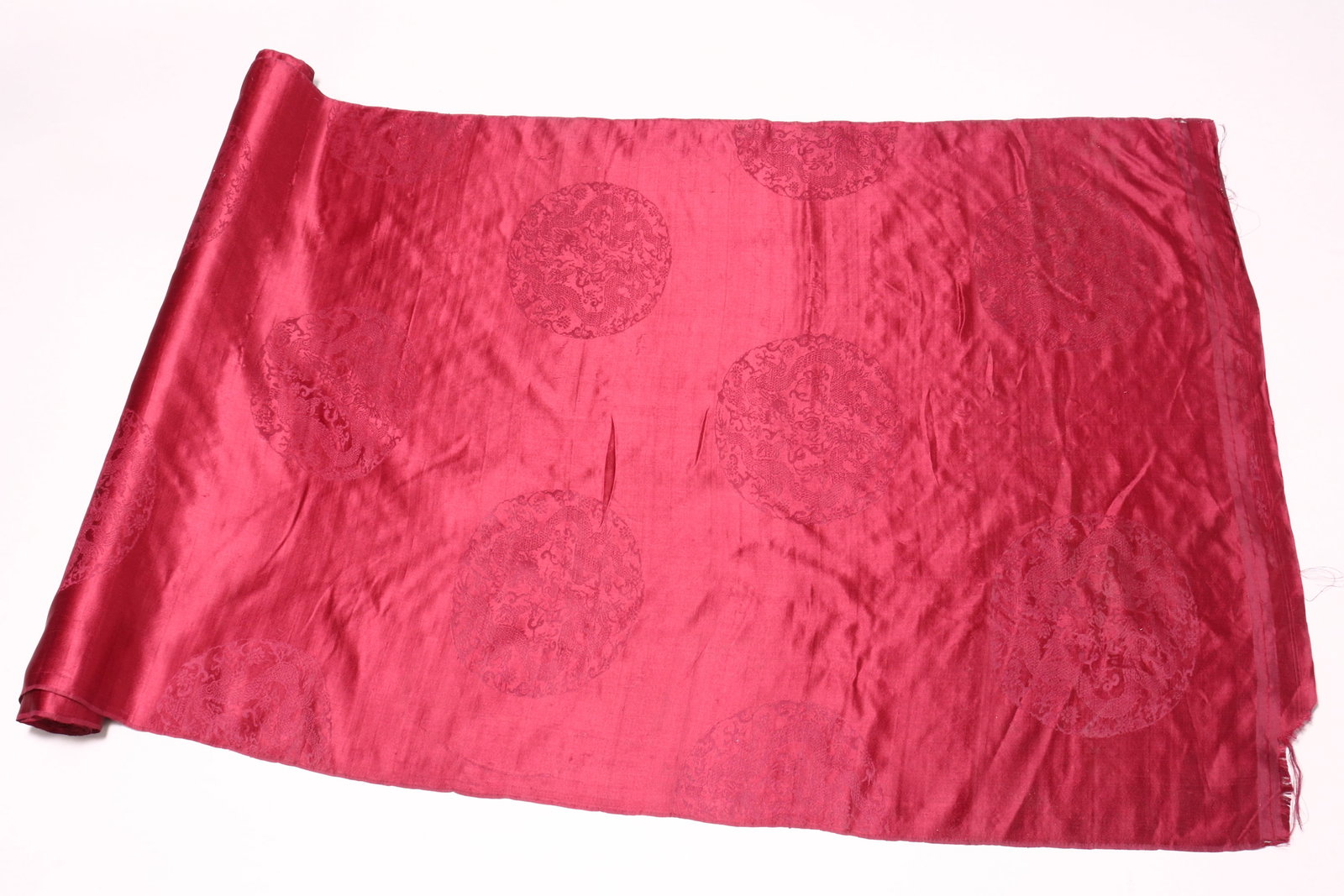 Chinese Length of Silk,: in rich burgundy decorated with shou dragon roundels, marked Suzhou Zhi Zao Chang, approximate length 696cm x 76cm