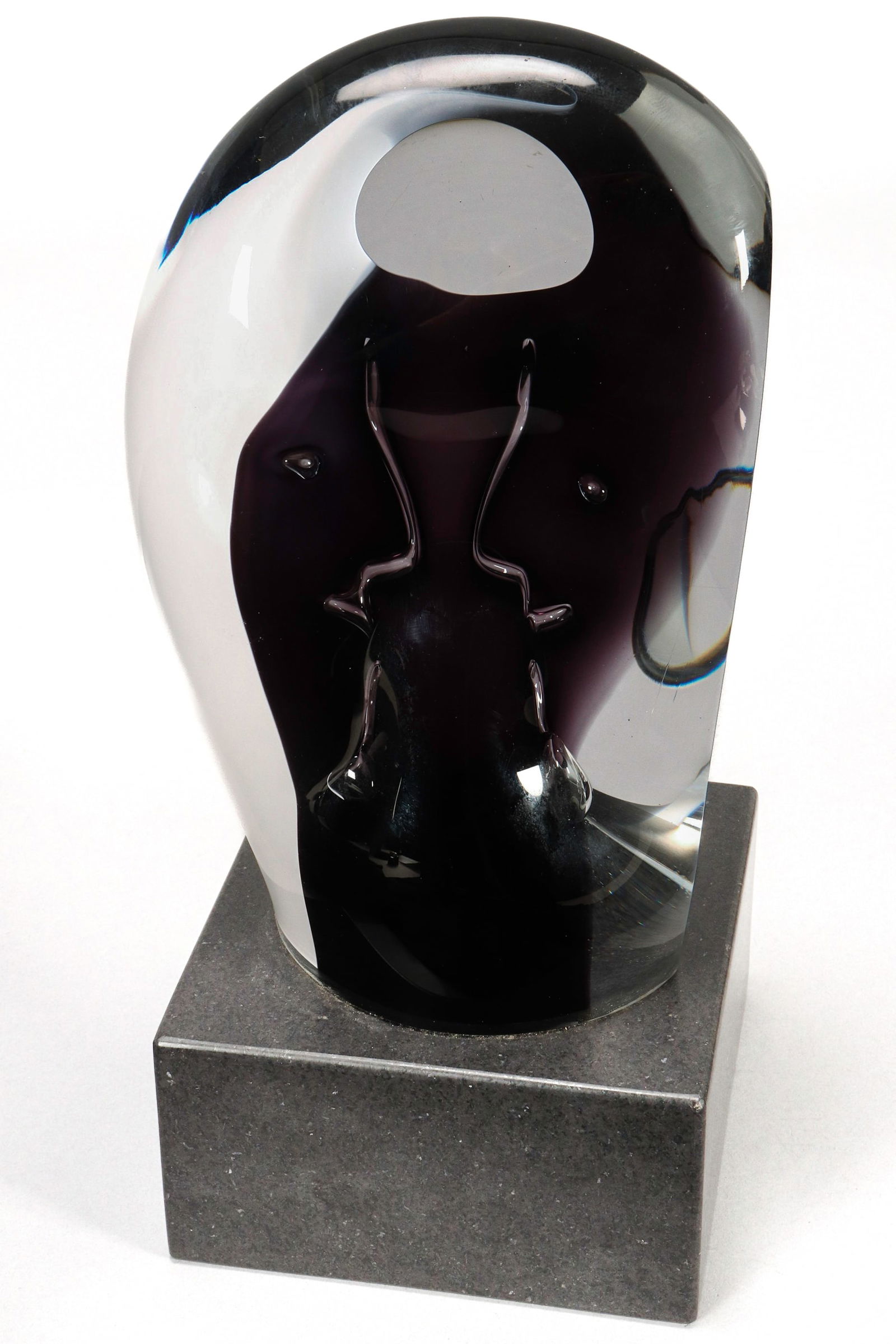 Goran Warff (1933-2022) Glass Sculpture,: for Kosta Boda, of oval form, depicting an abstract style face, in clear, purple, white and black glass, raised on a square black stone base, etched signature to base, height 33cm
