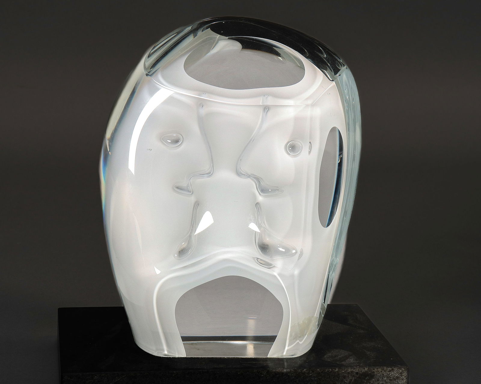 Goran Warff (1933-2022) Glass Sculpture,: for Kosta Boda, of oval form, depicting an abstract style face, in white and clear glass, raised on a rectangular black stone base, etched signature to base, height 26.5cm