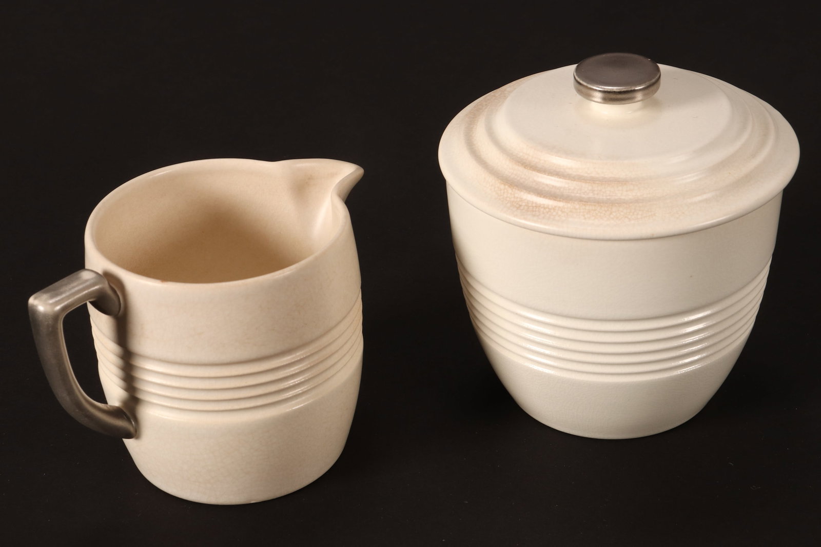 Wedgwood Keith Murray Moonstone Glaze Milk Jug and Covered Sugar Bowl,: c.1935, of ribbed cylindrical form, accented with silver finial and handle, height 9.5cm and 7cm (2)