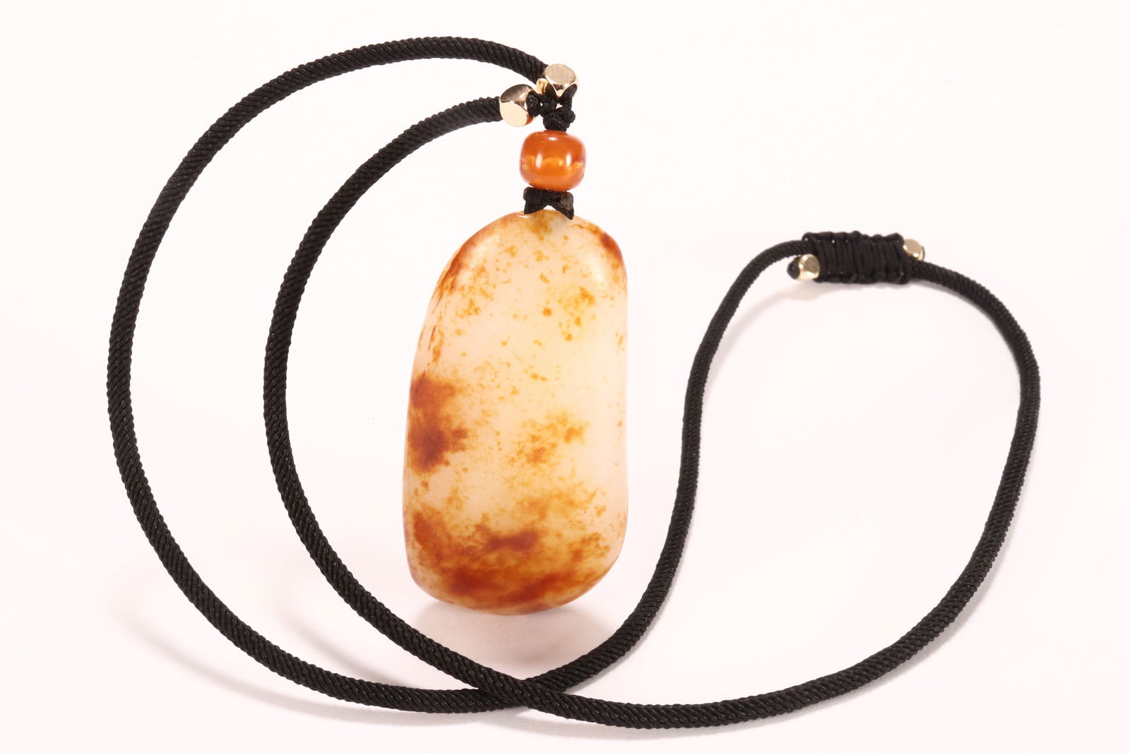 Chinese White Jade Pendant,: of organic form, set on a cord necklace with stone bead, in white tones with russet skin, pendant length 6cm