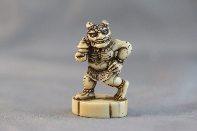 Good 18th Century Ivory Netsuke of an Oni, c.1750: depicted with muscular body and tiger skin breaches, the demon making off with a small shrine stolen from temple, partial British Antique Dealers Label verso,h 4cm