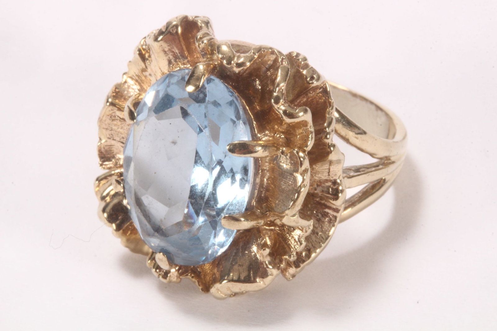 10ct Gold Gem Set Ring,: unmarked (acid tested minimum fineness 10ct), the setting of organic frilled form, bordering an oval cut blue stone testing as blue Spinel, measuring approx. 15mm x 12.27mm x 6.27mm, above a triple sp
