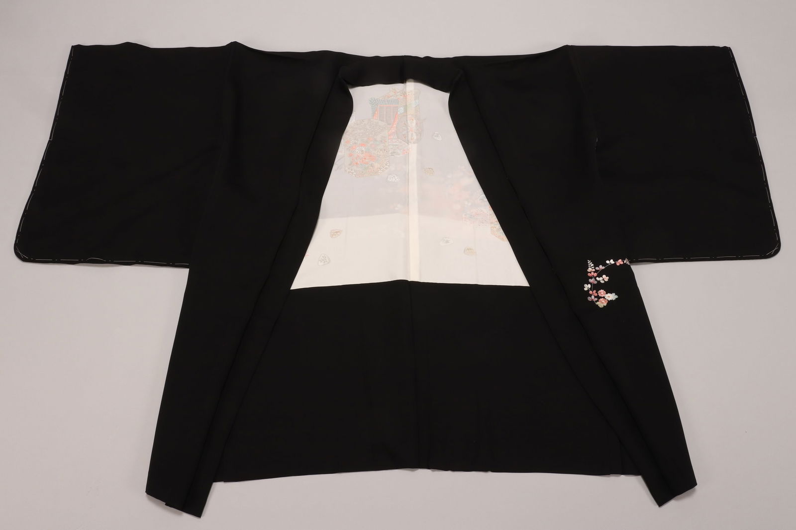 Japanese Haori,: the exterior decorated with blossoming foliate reserves to the back panel and sleeves, in soft polychrome tones on a black ground, the interior in white, painted with scene of imperial ox carts, in to