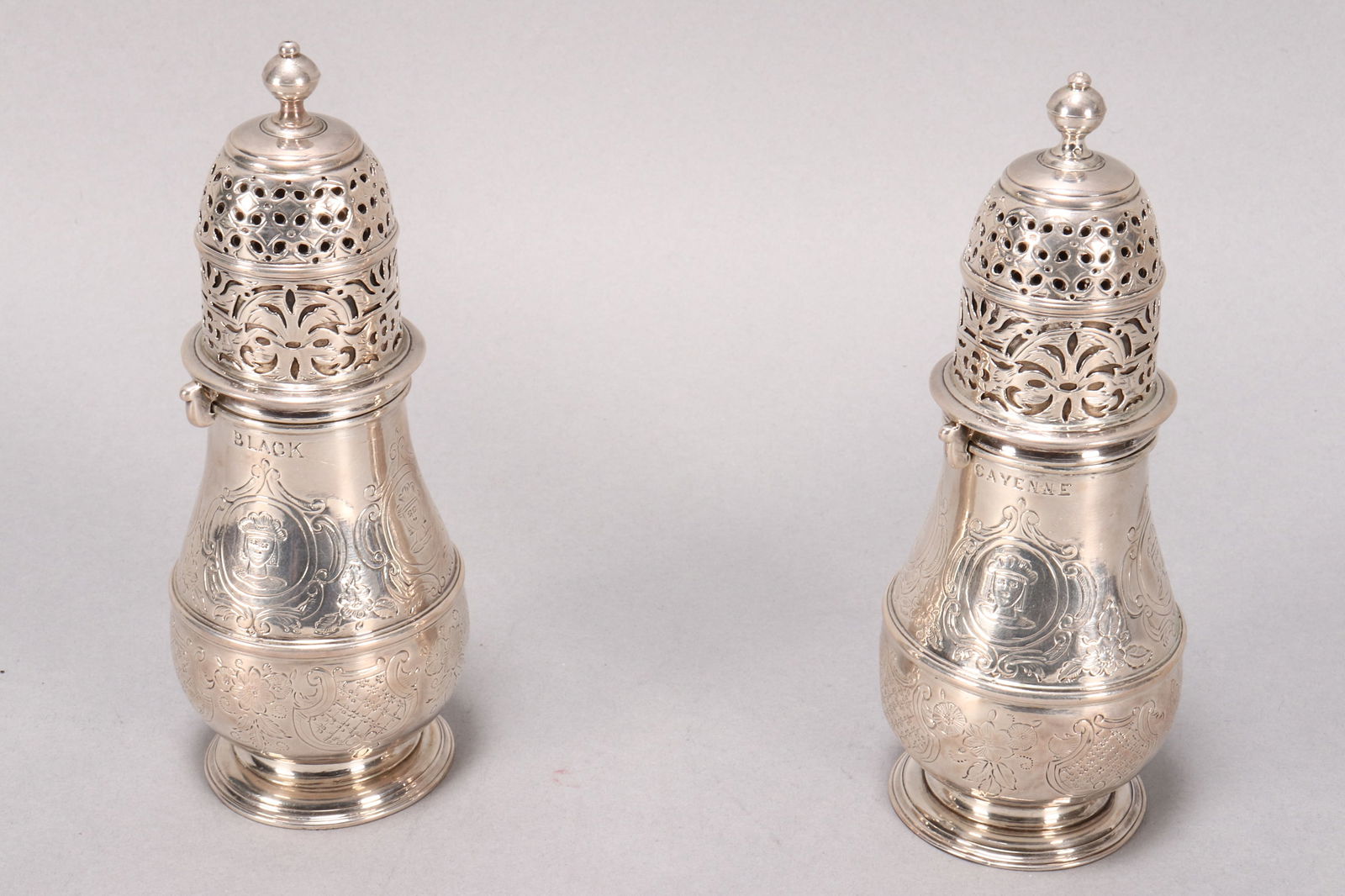 Rare Pair of Queen Anne Britannia Silver Casters,: hallmarked London, 1707, AD (Charles Adam), with spherical finials above a pierced cover, the baluster body engraved with c-scroll bordered reserves displaying lion crest and repeating portrait, one m