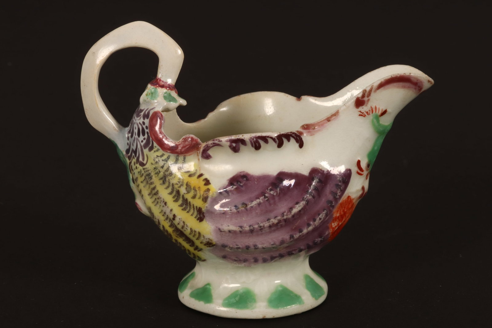 18th Century Worcester Dolphin Ewer/Cream Boat,: c.1765, decorated with shells in relief and entwined dolphins beneath spout, in tones of puce, green and yellow, a/f (repair to handle), height 8cm Provenance: Property of a Lady