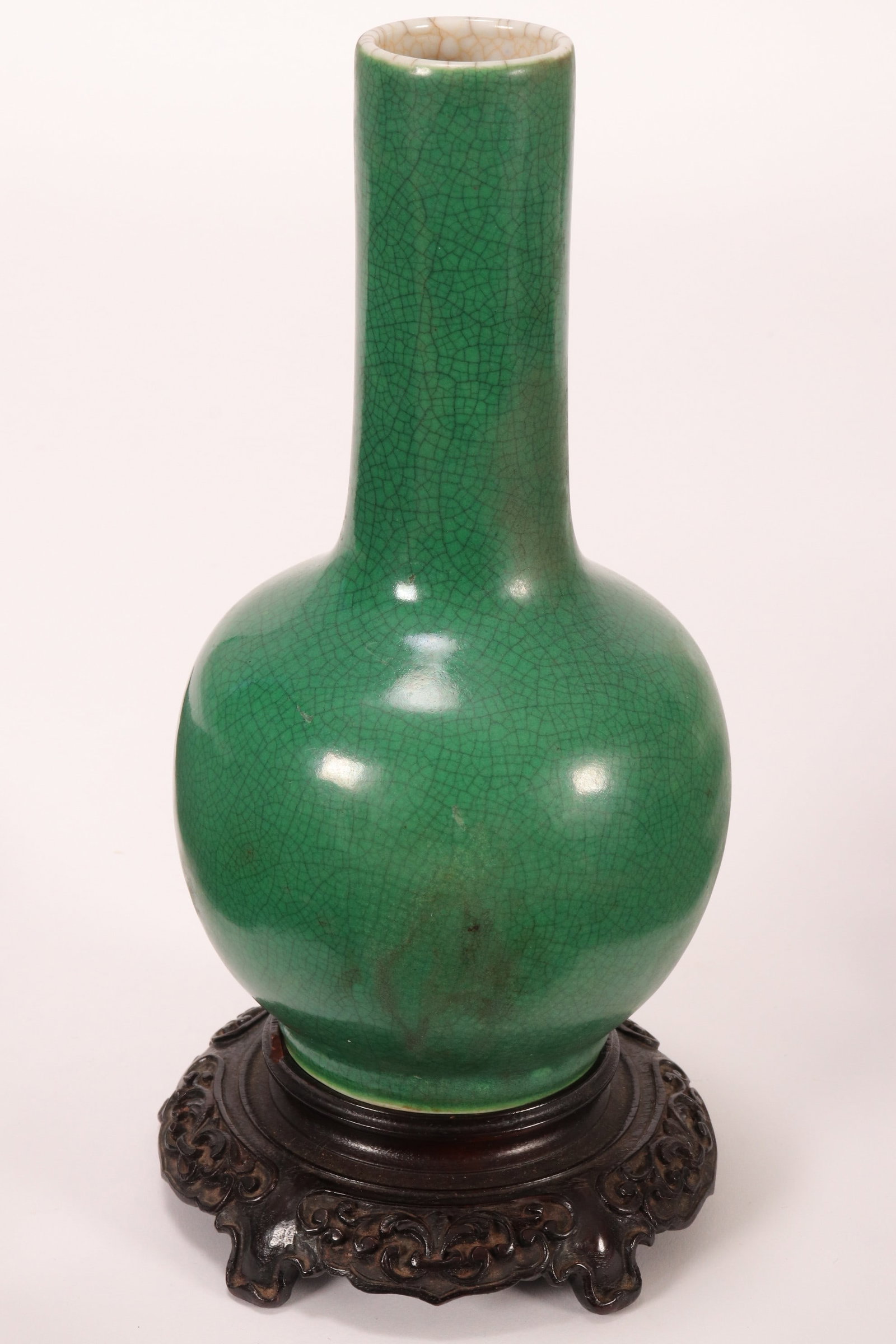 Chinese Qing Dynasty Apple Green Crackle Glaze Bottle Vase,: possibly Kangxi Period, with cylindrical neck and baluster body, raised on a circular foot marked Kangxi to base, on a carved wooden stand, a/f, height 23cm and 26cm (including stand) Similar: Bonhams