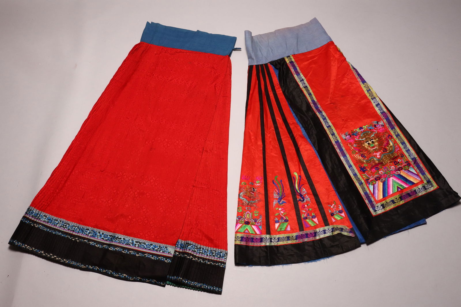Two Chinese Late Qing Dynasty Skirts,: the longer example in red silk concertina, with central panels, edged with San Lan embroidery and decorated with two cutwork foliate reserves on a red silk ground, with blue cotton waistband secured w