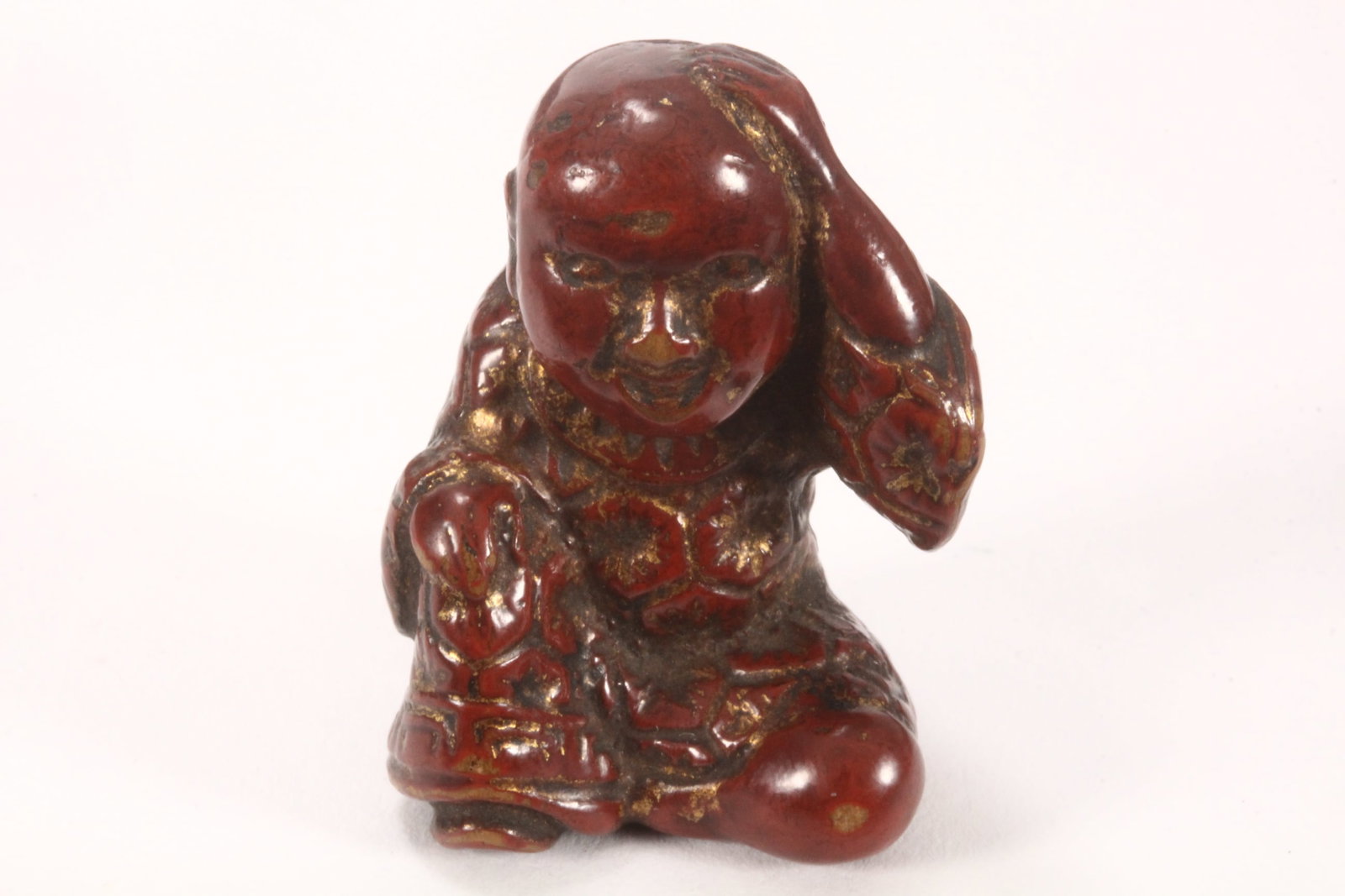 Japanese Meiji Period Lacquered Netsuke,: depicting a man kneeling with one hand raised on his head, with honey comb design to robe and evidence of gilt, height 4cm