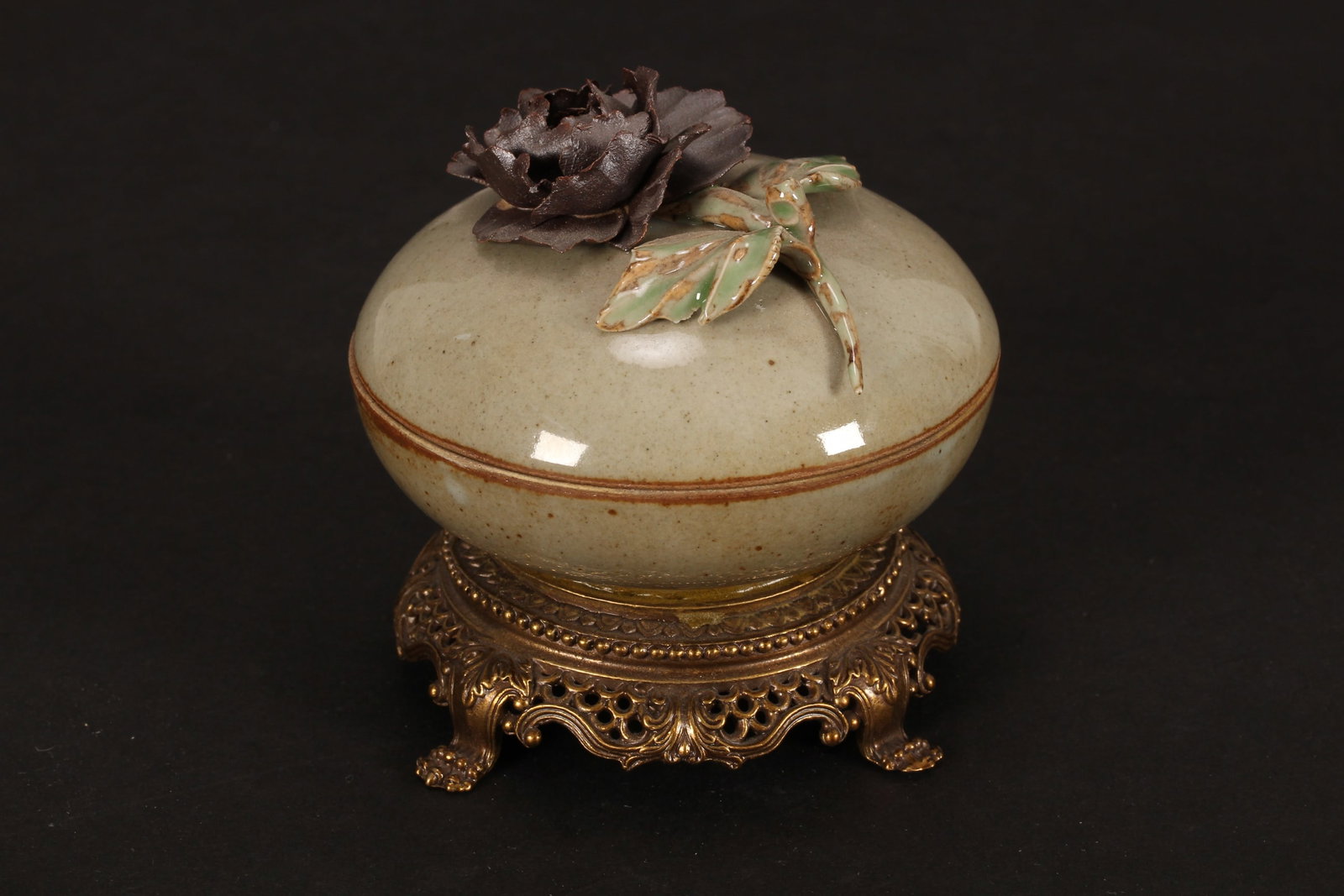 Chinese Porcelain and Gilt Metal Box and Cover,: of squat globular form, set with applied flower to cover, above a mottled pale green glaze, on a pierced gilt metal base, standing on four paw feet, height 8.5cm and diameter 9cm