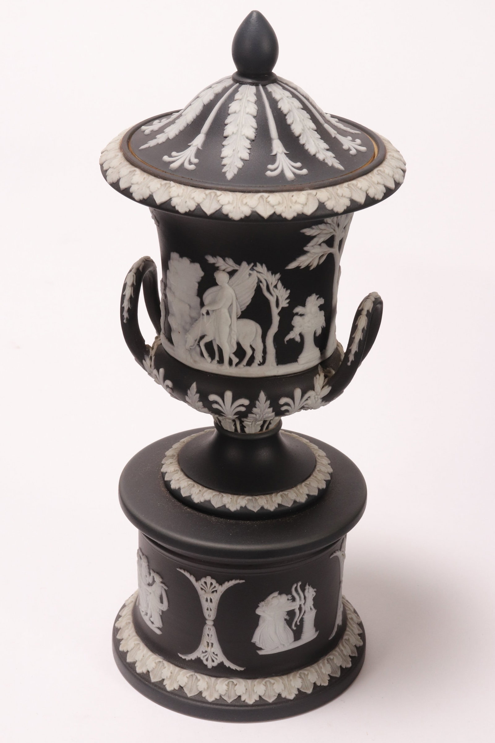 Wedgwood Jasperware Lidded Urn on Stand,: early 20th Century, dated 1905, the domed cover with pointed finial, above a twin handled urn, decorated with classical figures in an outdoor setting, raised on a pedestal base, in white on black, imp