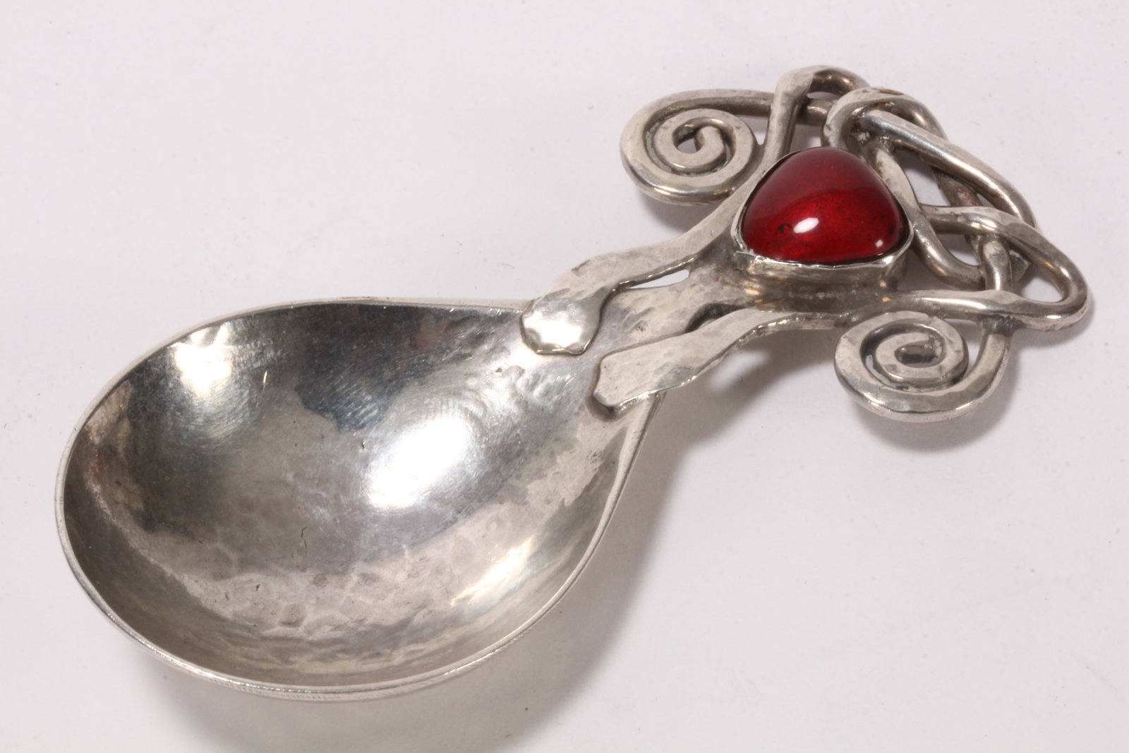Rare Arts and Crafts Sterling Silver Caddy Spoon,: hallmarked London, 1905, R.N & C.R (Omar Ramsden & Alwyn Carr), set with red enamel cabochon surrounded by scrolls and entwined work, with deep bowl in a hand beaten finish, total weight 34g, length 8