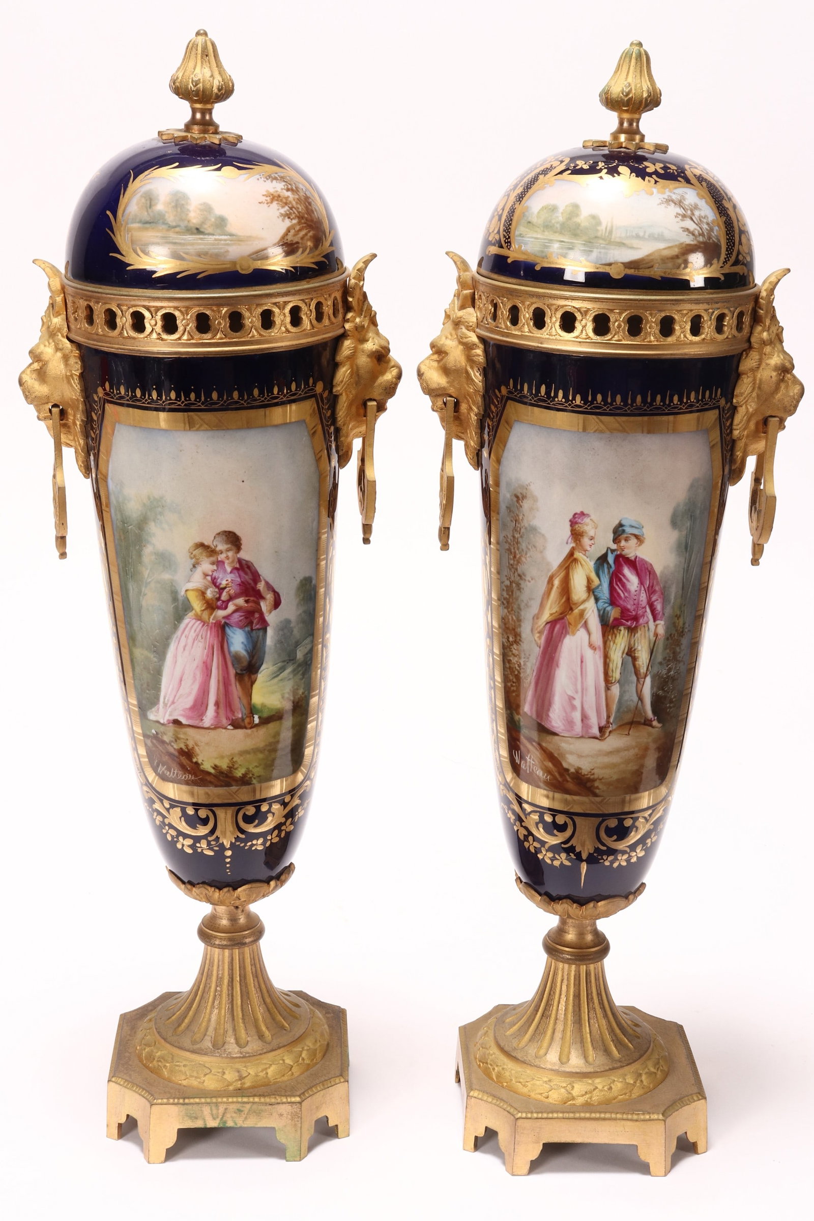 Large Pair of Sevres Style Porcelain and Gilt Brass Lidded Urns,: the domed cover set with acorn finial, above a tapered body with twin gilt lion mask handles, beautifully painted with gilt bordered Watteauesque scene of a courting couple, with landscape scene verso