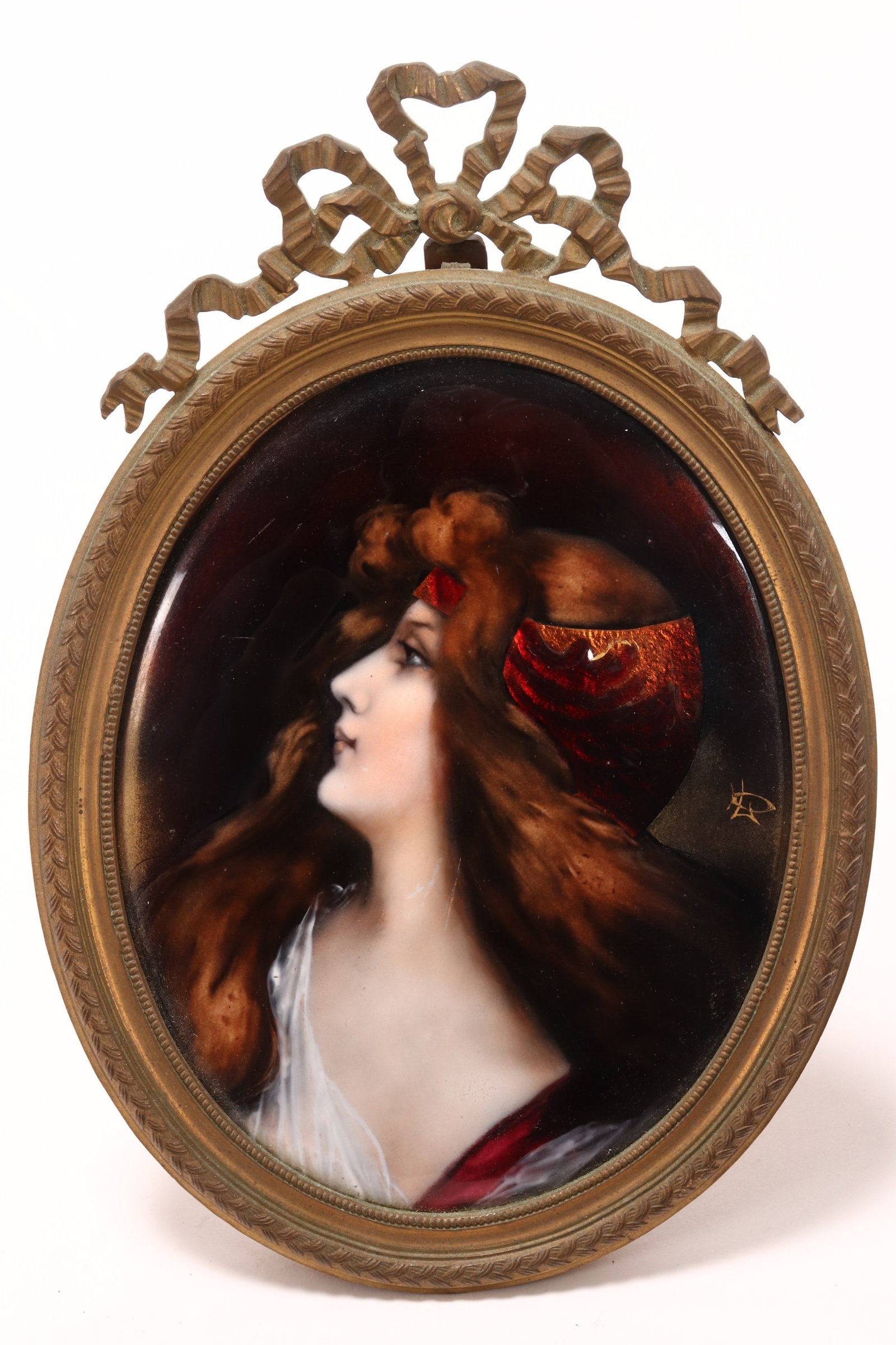 Late 19th/20th Century Limoges Enamel Portrait,: of oval form, depicting a woman in three quarter sinister with scarf in sweeping hair, in rich tones of red, aventurine, white and brown, monogram to edge, within oval frame with ribbonned crest rail,