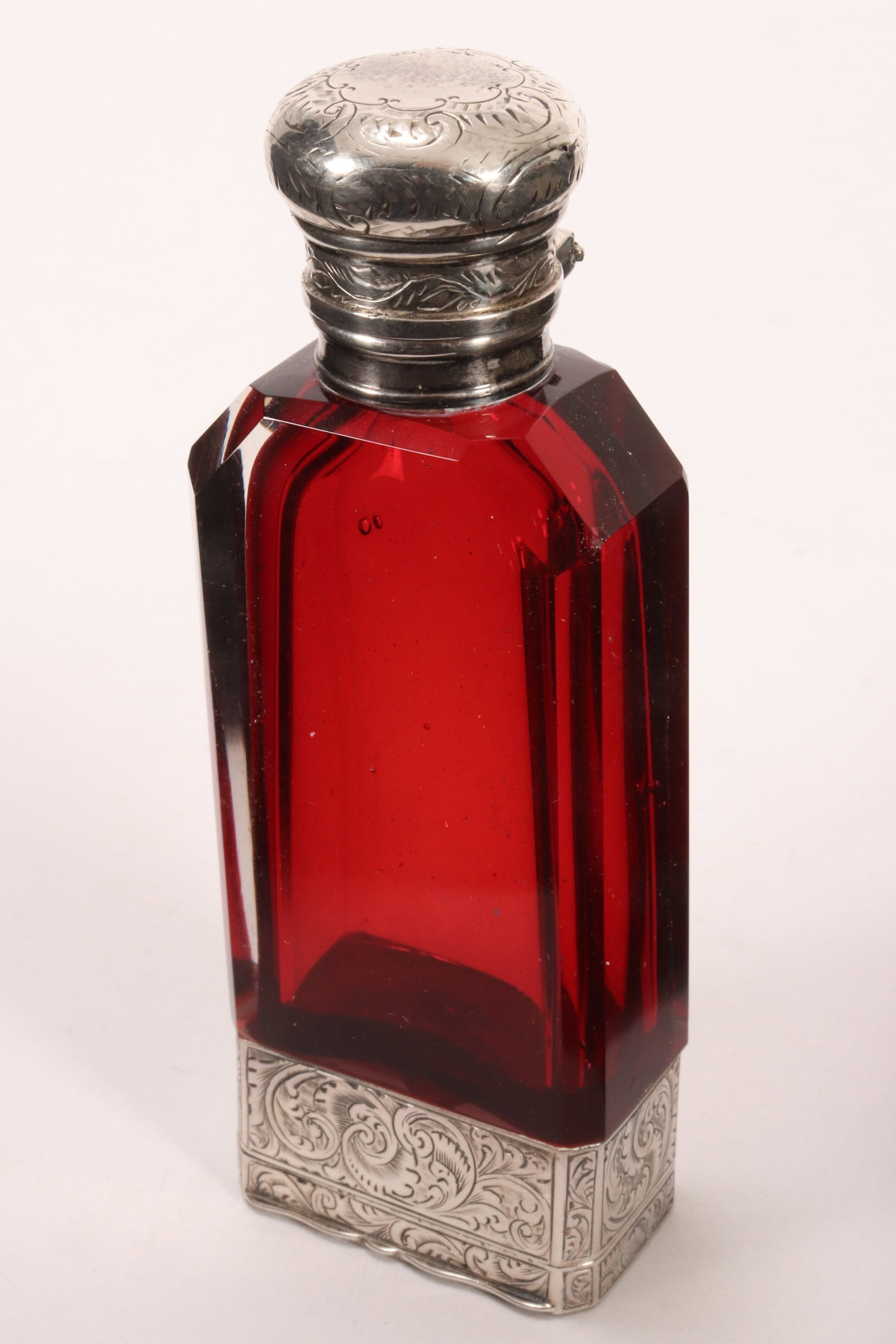 Victorian Sterling Silver and Ruby Glass Combination Scent Bottle and Vinaigrette,: hallmarked Birmingham, R.N, of rectangular form with sloping shoulders, the hinged cover set with glass stopper, the lower section with hinged cover to reveal pierced grill, with engraved scrolling ac