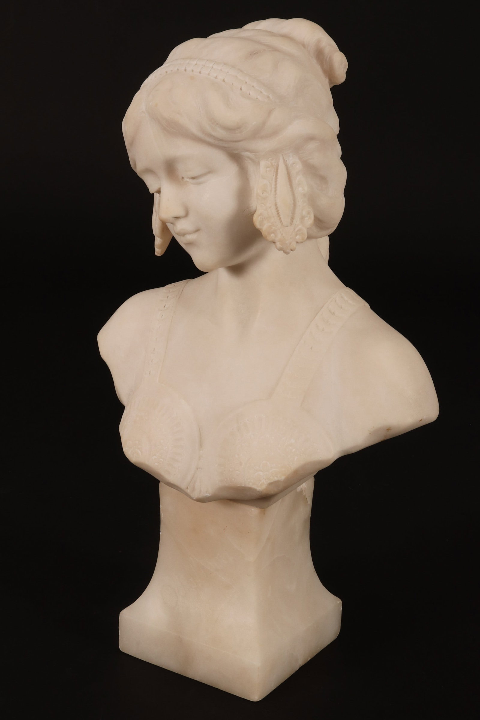 20th Century French Alabaster Bust,: depicting a woman, with curled hair adorned with beaded headdress and pleasant downward gazing expression, set above a sloping square base, height 37cm