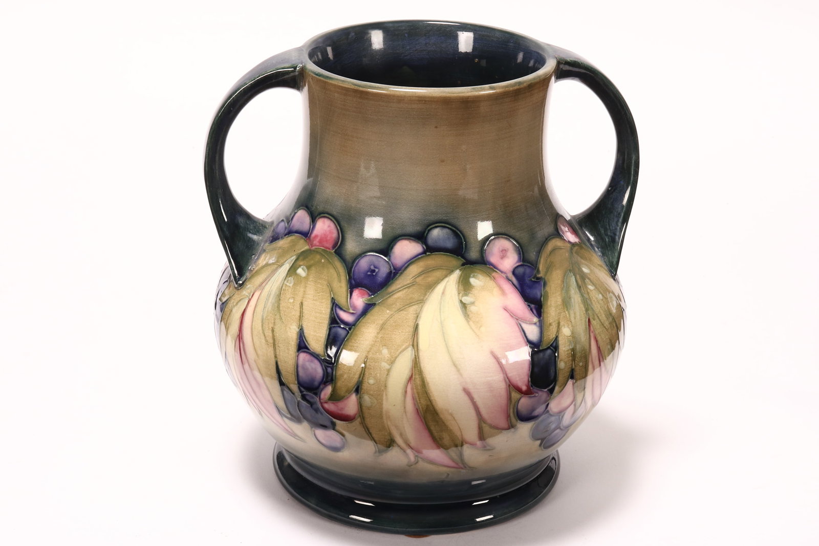 William Moorcroft 'Leaf and Berry' Twin Handled Vase,: of baluster form, the body decorated with a continuous trailing frieze of leaves and berries, in tones of pink, purple and pale green on a blue ground, signed and impressed marks to base, a/f, height 