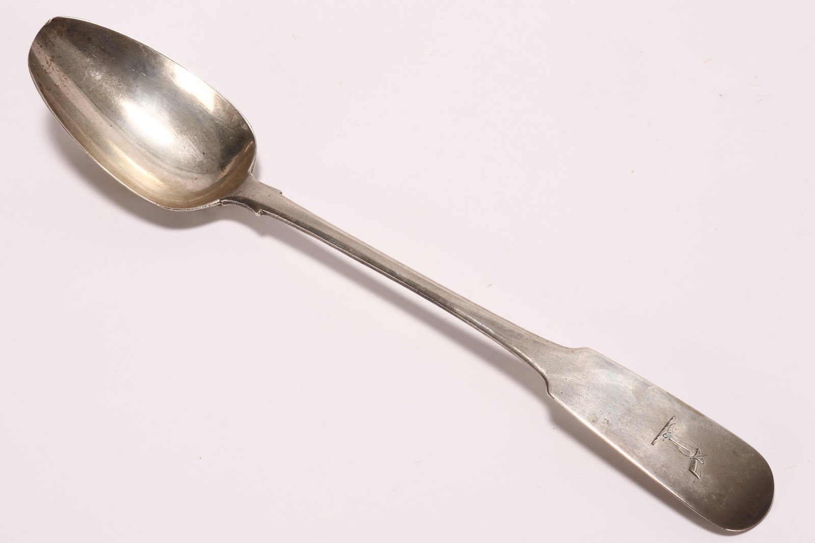 Irish George III/IV Sterling Silver Basting Spoon,: hallmarked Dublin, 1820, makers mark rubbed, in fiddle pattern, with engraved crest depicting a leg in armour to terminal, a/f (wear to tip of bowl), total weight 124g, length 31cm