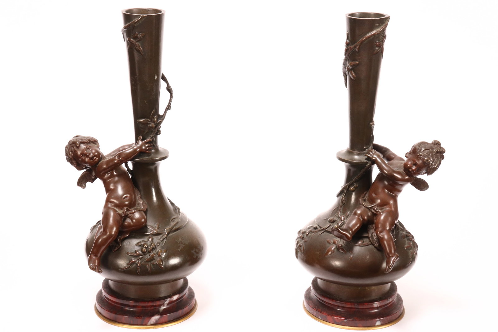 Pair of Bronze Putti Vases,: each with an elongated pear body, cast in relief with fruiting vine, the shoulder set with seated putto figure, above a stepped rouge marble base, marked 'Auguste Moreau' to body, height 26.5cm (2)