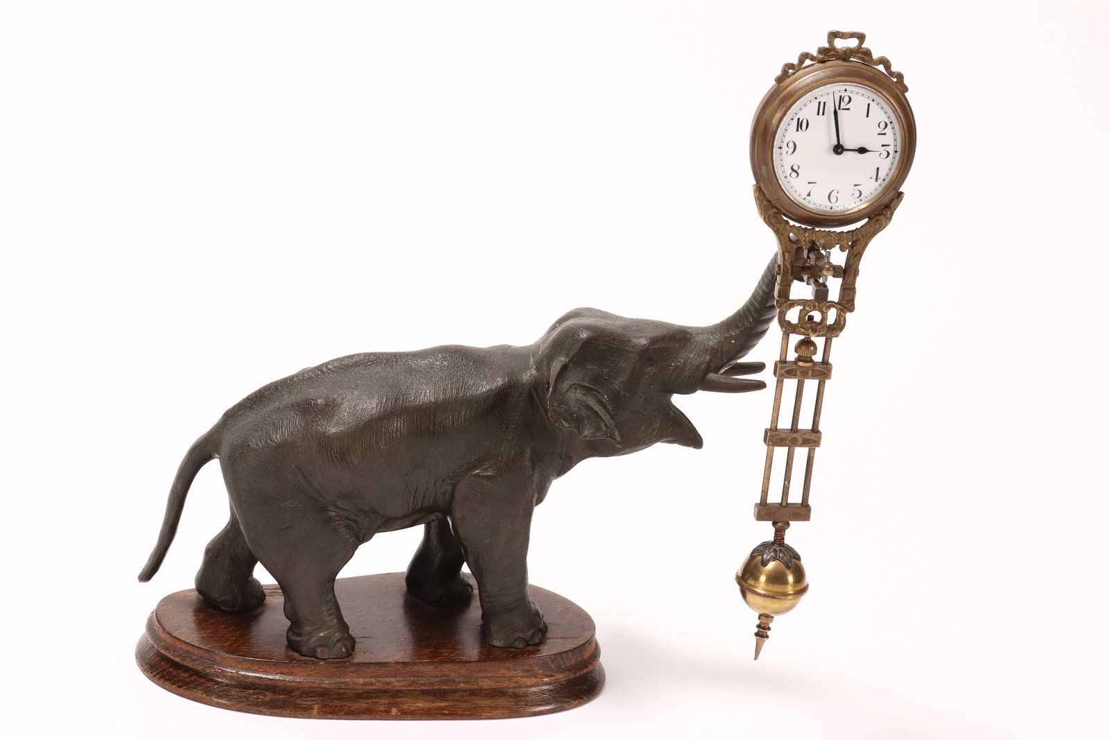 German Junghans Figural Elephant Mystery Clock,: in the form of an elephant with raised trunk, suspending a white enamel dial with Arabic numerals and gilt pendulum, raised on a wooden oval base, height 28.5cm and length 22.5cm
